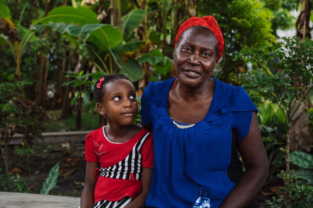 A woman in blue sits beside a girl in red.